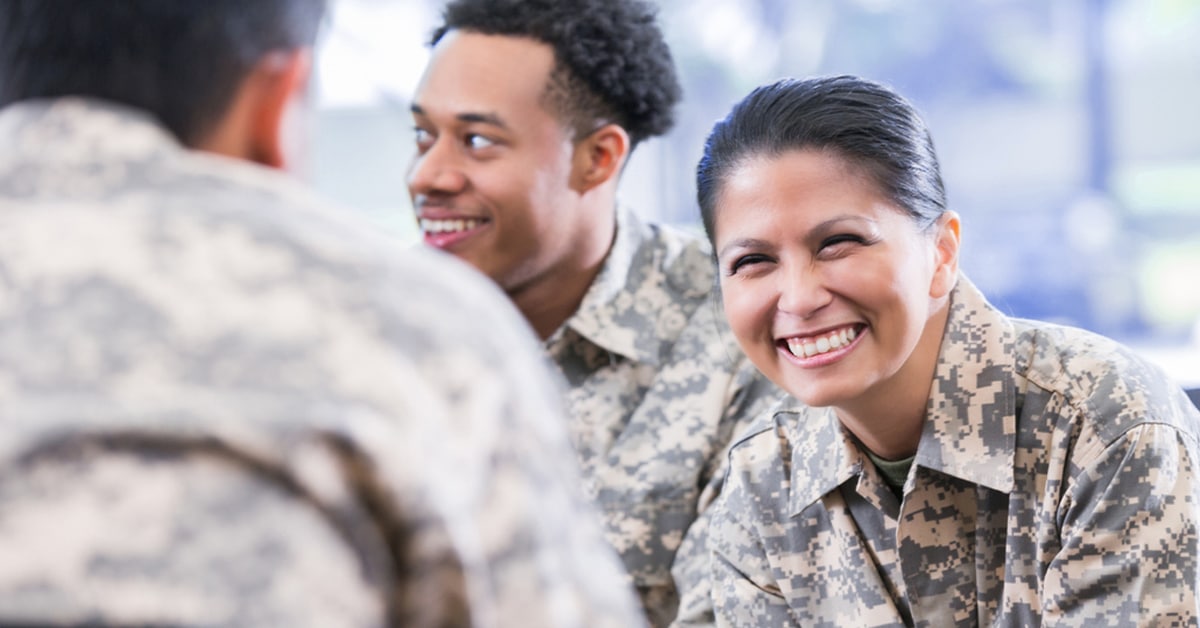 Smiling soldiers in camouflage uniforms having a conversation indoors.