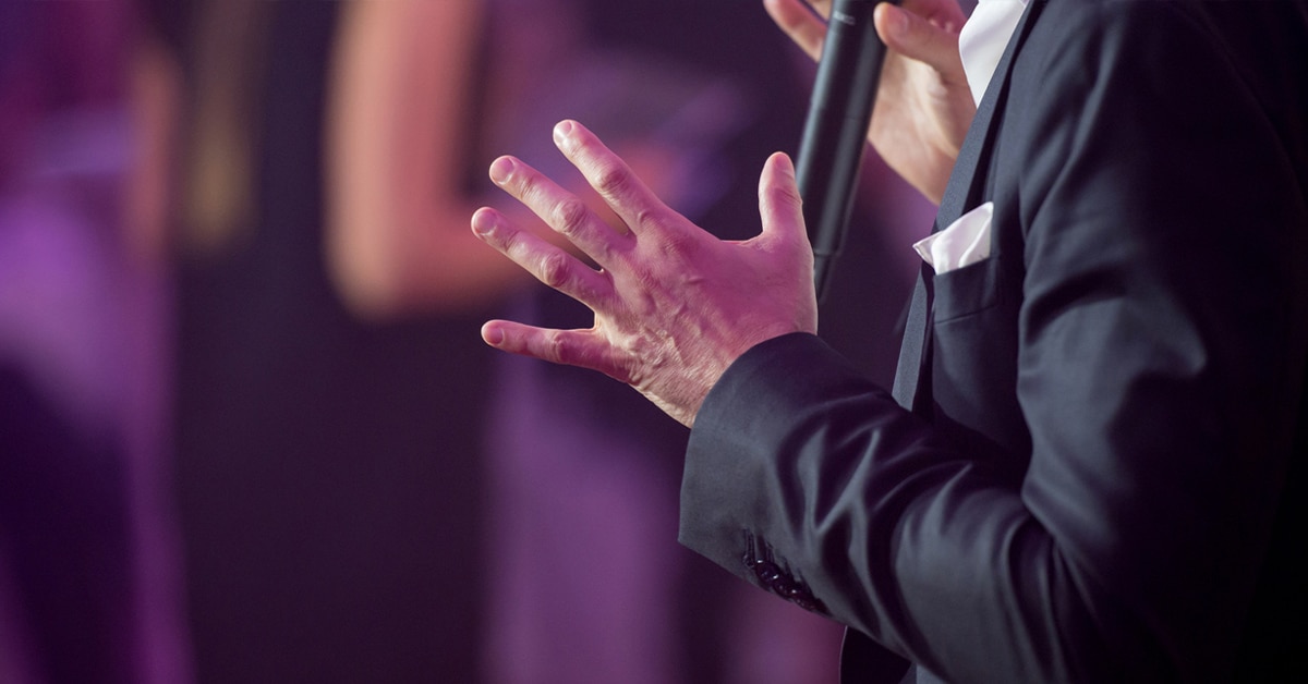 A person in a suit using a microphone at an event.