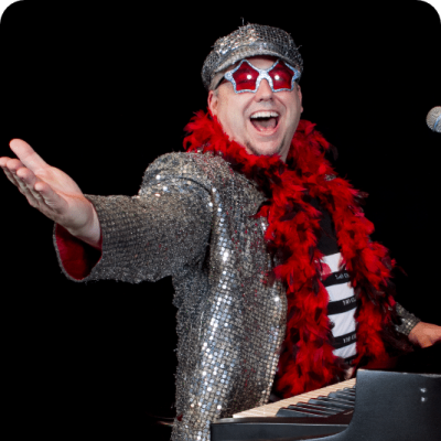 A performer in a sequined outfit and red feather boa playing piano on stage.