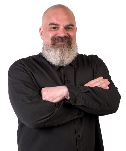 A smiling man with a beard and crossed arms in a black shirt.