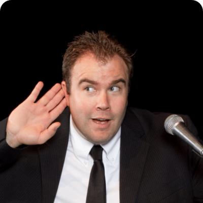 A man in a suit gestures while speaking into a microphone.